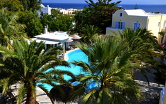 Hotel mit Pool, umgeben von Palmen, auf Santorin mit Meerblick im Hintergrund.