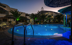 Beleuchteter Hotelpool bei Dämmerung, umgeben von Palmen und Gebäuden.