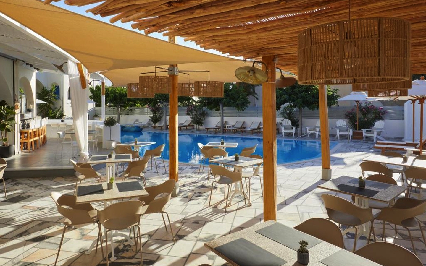 Offener Hotelbereich mit Pool, Tischen und Sonnenschutz in Santorin, Griechenland.
