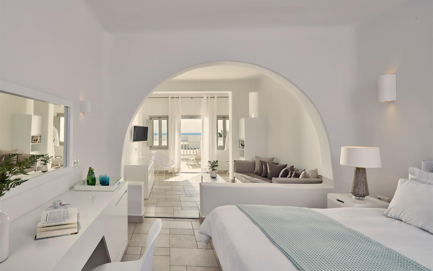 Helles Hotelzimmer mit Blick auf Terrasse und Meer in Santorin, Griechenland.