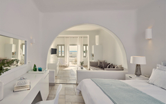 Helles Hotelzimmer mit Blick auf Terrasse und Meer in Santorin, Griechenland.