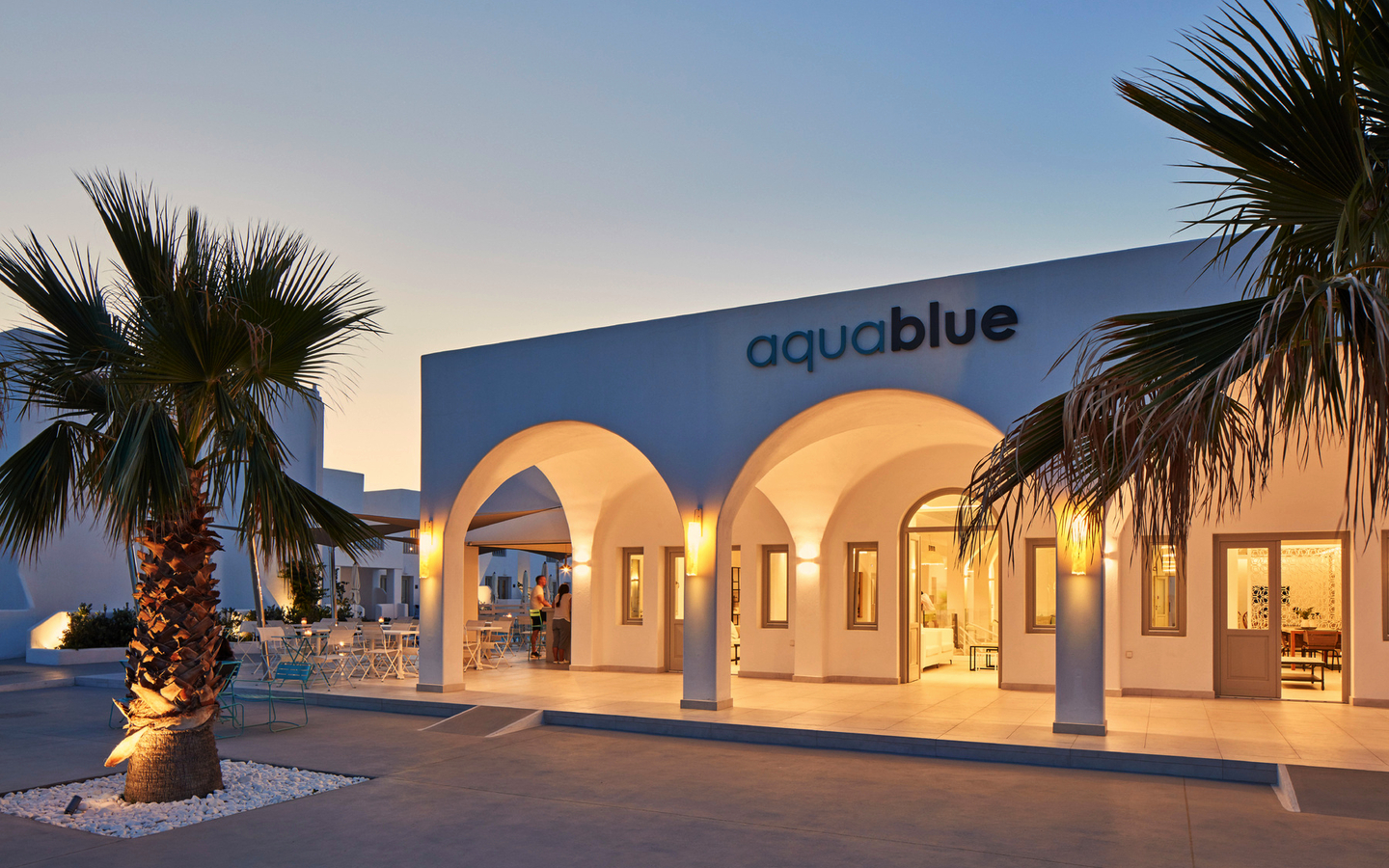 Außenansicht des Hotels Aqua Blue auf Santorin, beleuchtet in der Abenddämmerung.