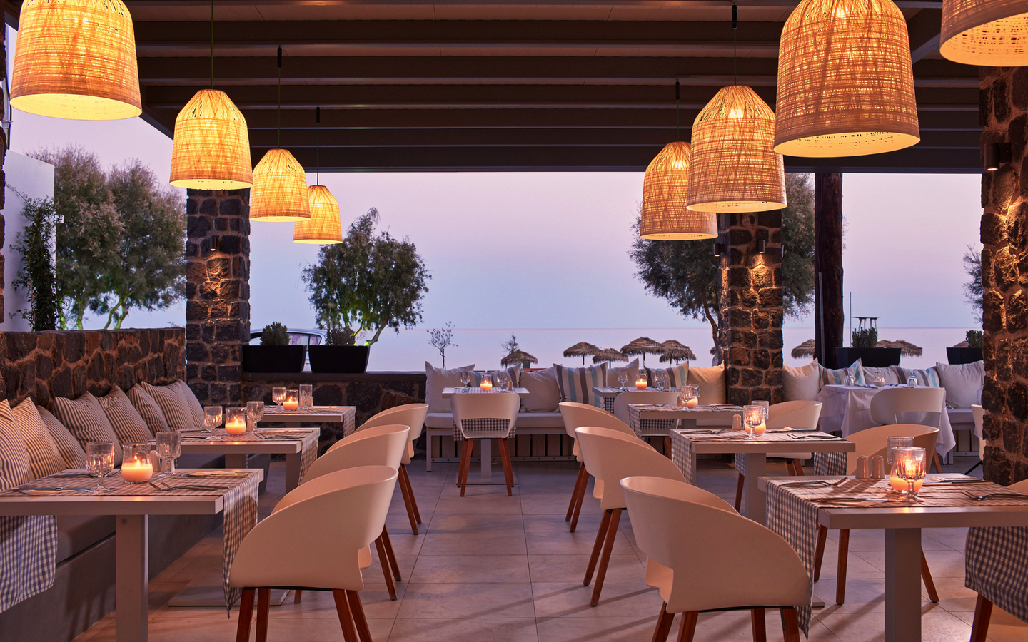 Außenbereich eines Restaurants mit Kerzenbeleuchtung und Blick aufs Meer bei Sonnenuntergang.
