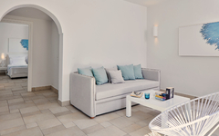 Helles Hotelzimmer mit Sofa, Couchtisch und Wandkunst in blauem Farbschema.