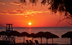 Strand bei Sonnenuntergang mit Liegen und Strohdächern, Santorin, Griechenland