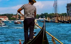 Gondoliere steuert Gondel auf Kanal in Venedig bei sonnigem Wetter.