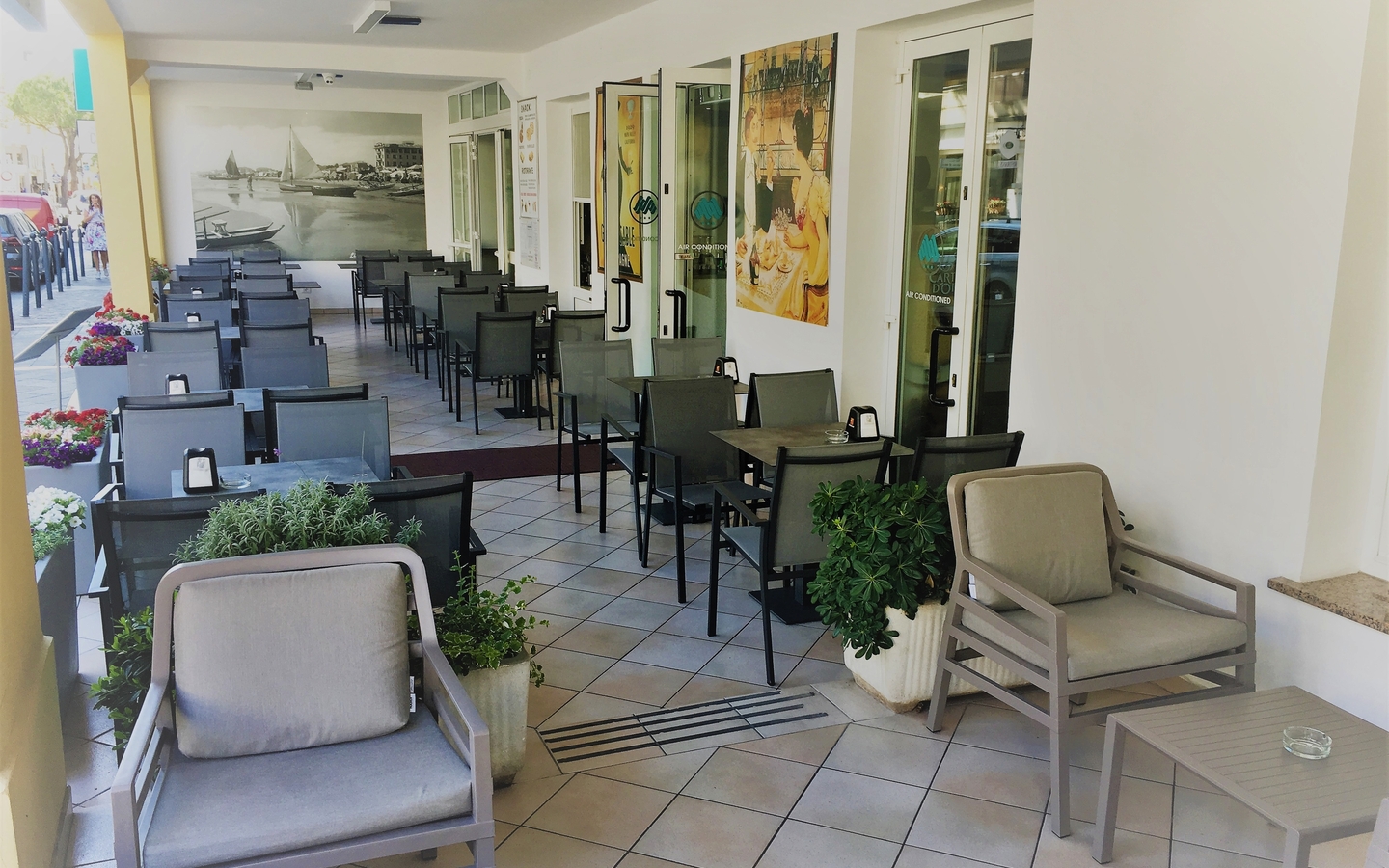 Terrasse eines Hotels mit Stühlen und Tischen, Pflanzen und Wandbildern.