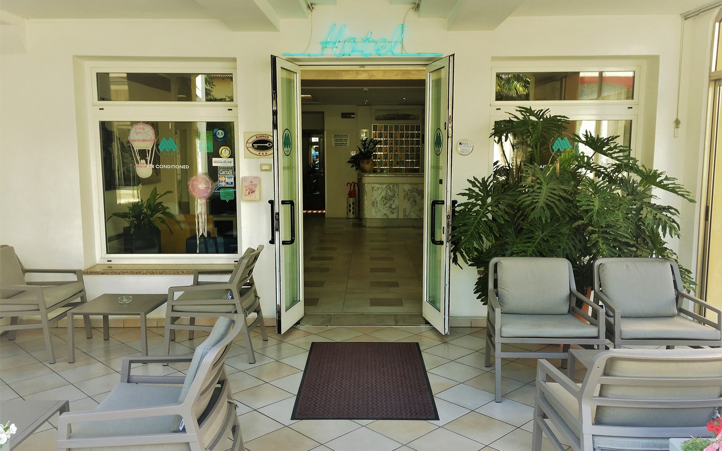 Eingang eines Hotels mit Sitzgelegenheiten und Pflanzen im Vordergrund.