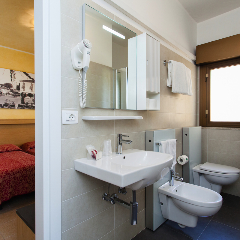 Badezimmer eines Hotelzimmers mit Waschbecken, Bidet und Dusche, im Hintergrund ein Bett.