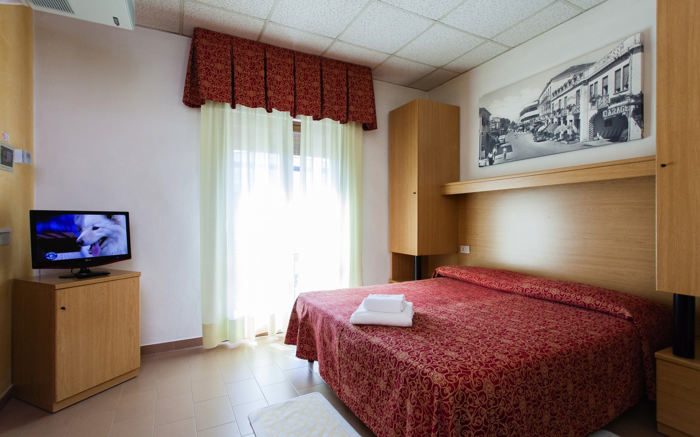 Hotelzimmer mit Doppelbett, Fernseher, Kunst an der Wand und Tageslicht durch ein Fenster.