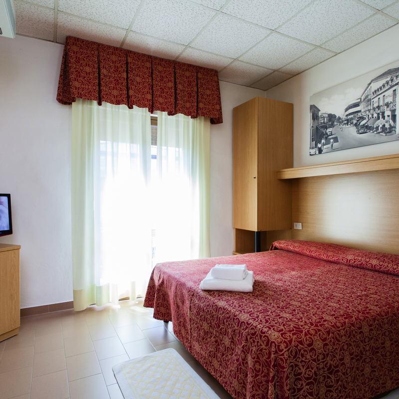 Hotelzimmer mit Doppelbett, Fernseher, Kunst an der Wand und Tageslicht durch ein Fenster.