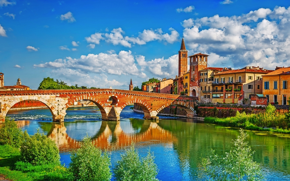 Historische Brücke über Fluss in malerischer Stadt mit Kirchturm und bunten Häusern.