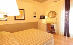 Hotelzimmer mit Doppelbett, Schreibtisch, Spiegel und Lampe in warmem Licht.