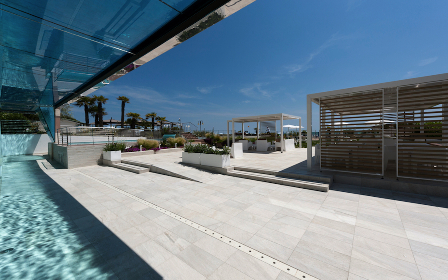 Hotelpool im Freien mit modernen Sitzbereichen unter freiem Himmel und Palmen im Hintergrund