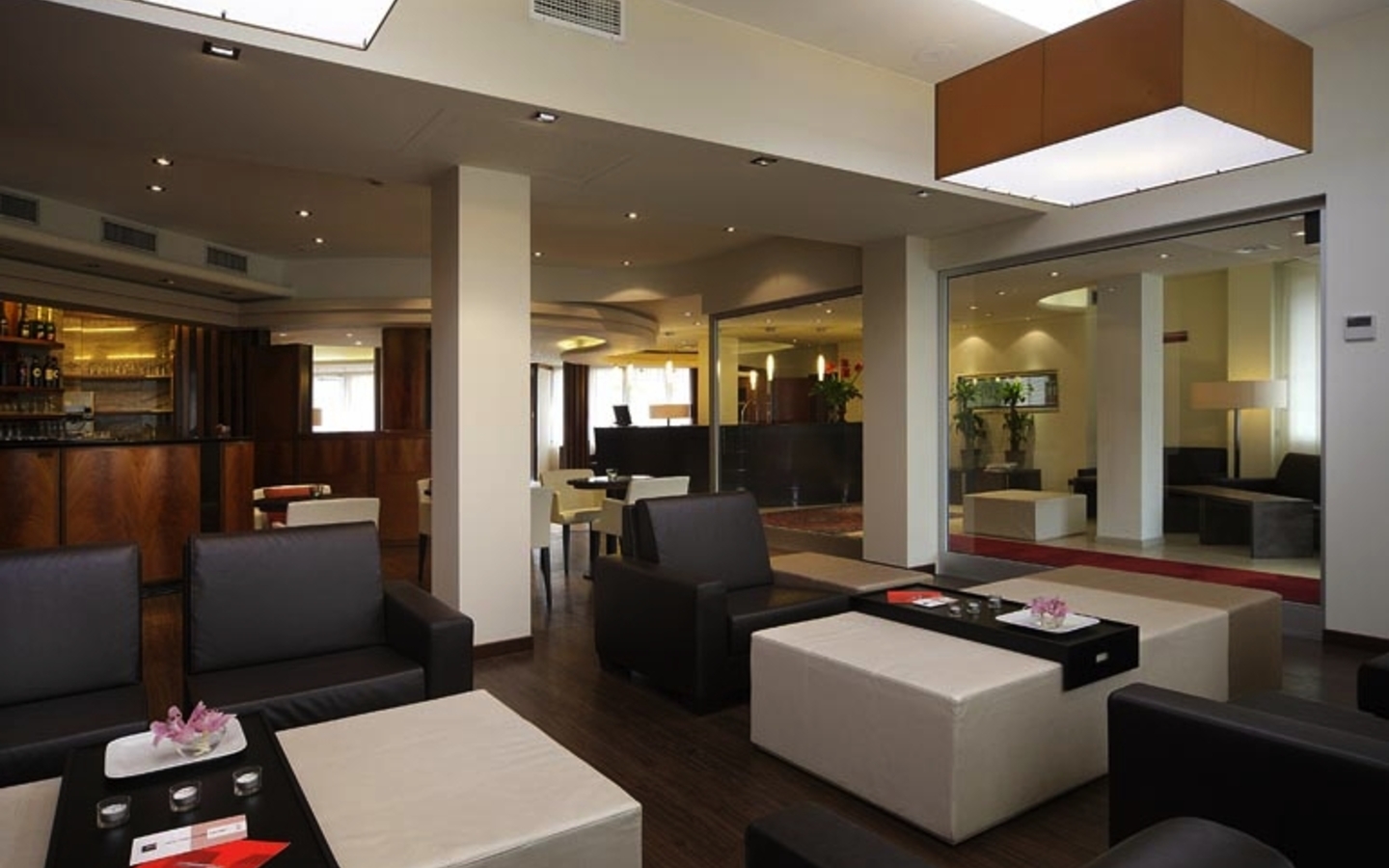 Moderne Hotellobby mit Sitzgelegenheiten, Tischen und einer Bar im Hintergrund.