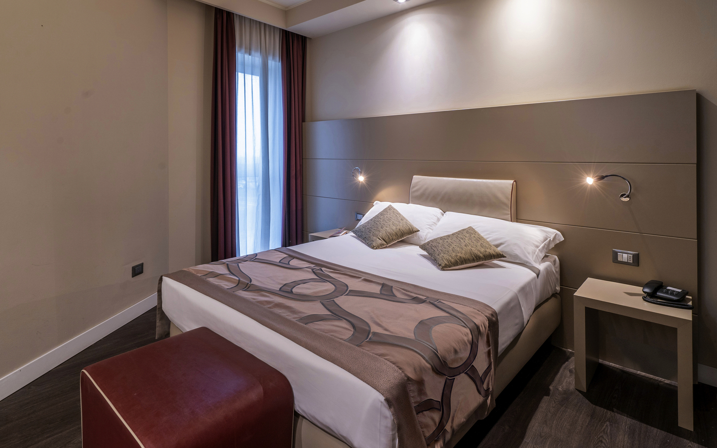 Modernes Hotelzimmer mit Doppelbett, Nachttisch und Schreibtischlampe.