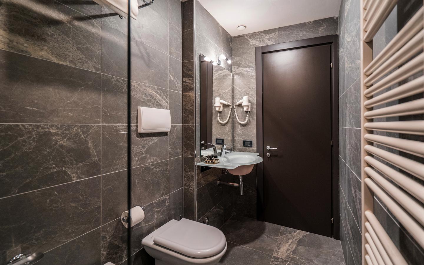 Modernes Hotelbadezimmer mit grauen Fliesen, Waschbecken und Toilette in Venedig.