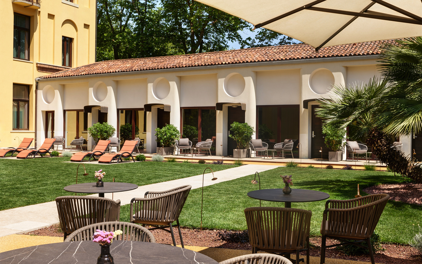 Gartenbereich eines Hotels mit Tischen, Stühlen und Liegestühlen.