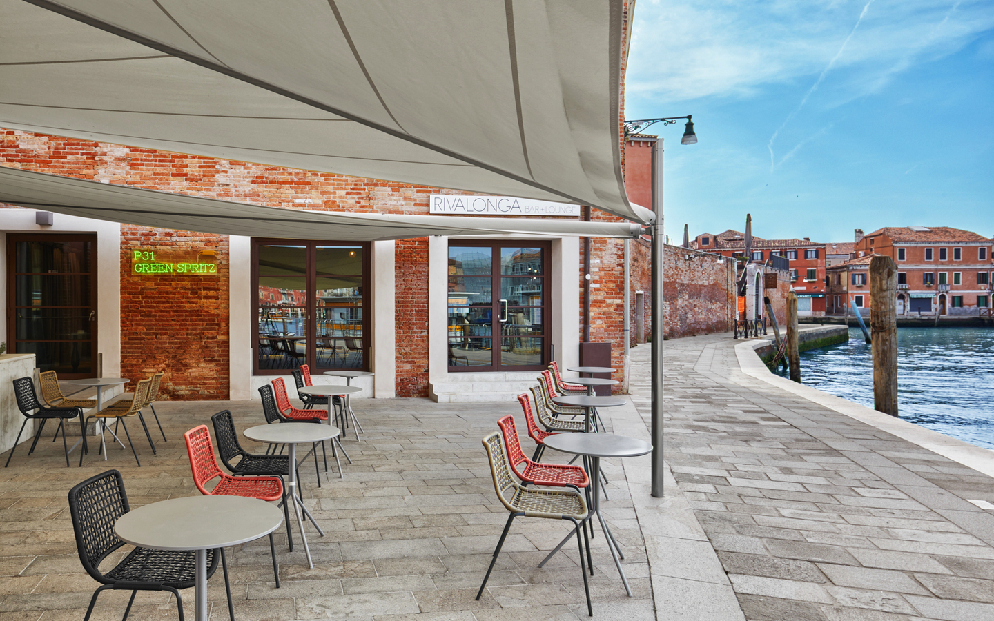 Außenbereich eines Cafés am Wasser mit Tischen und Stühlen, sonniger Tag.