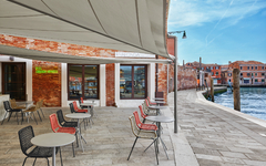 Außenbereich eines Cafés am Wasser mit Tischen und Stühlen, sonniger Tag.