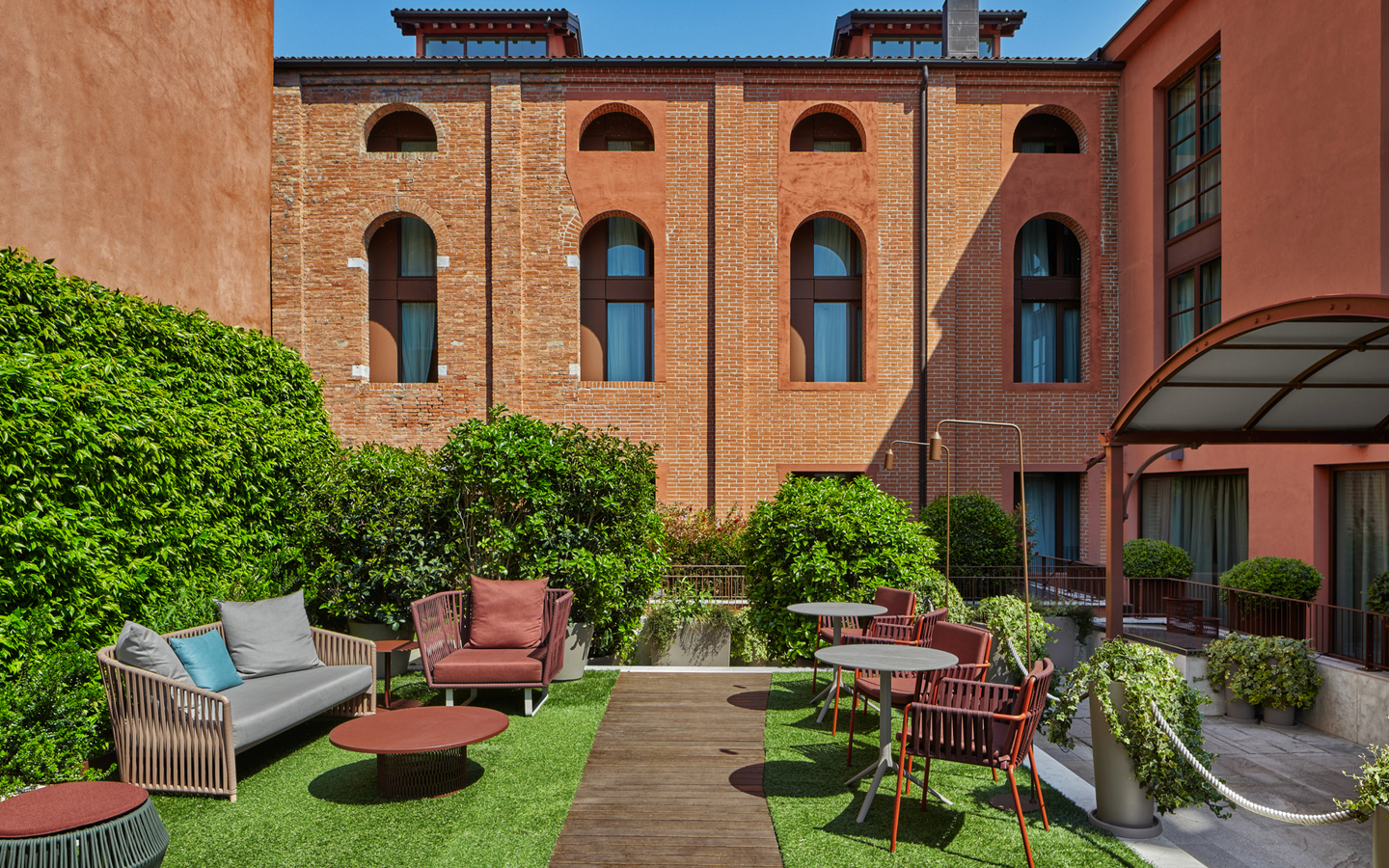 Lounge im Hyatt Centric Murano Venice mit Sitzmöbeln und Pflanzen im Freien.