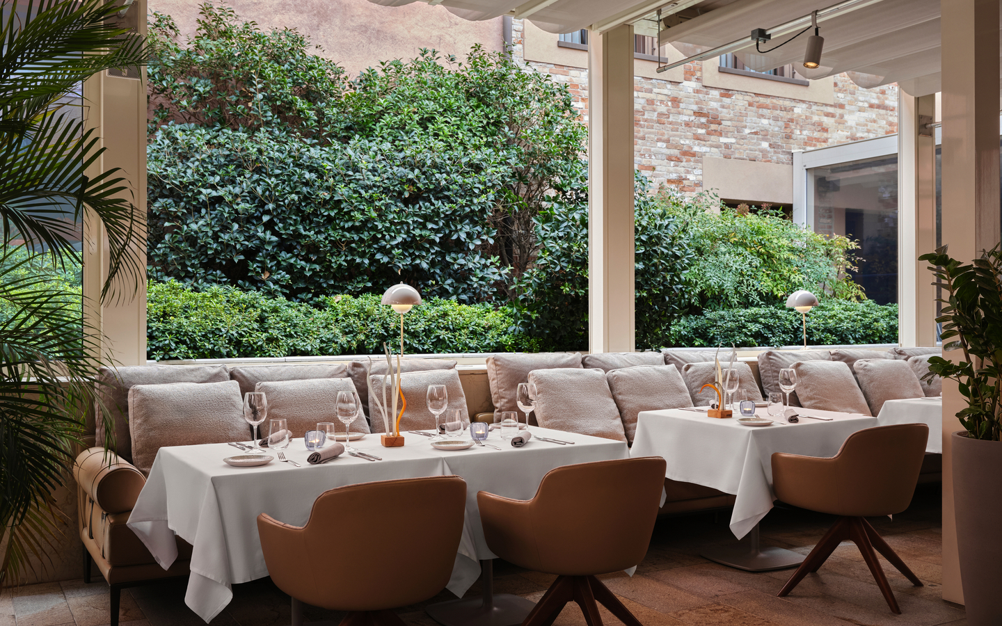Außenbereich eines Restaurants mit gedeckten Tischen und grüner Umgebung.