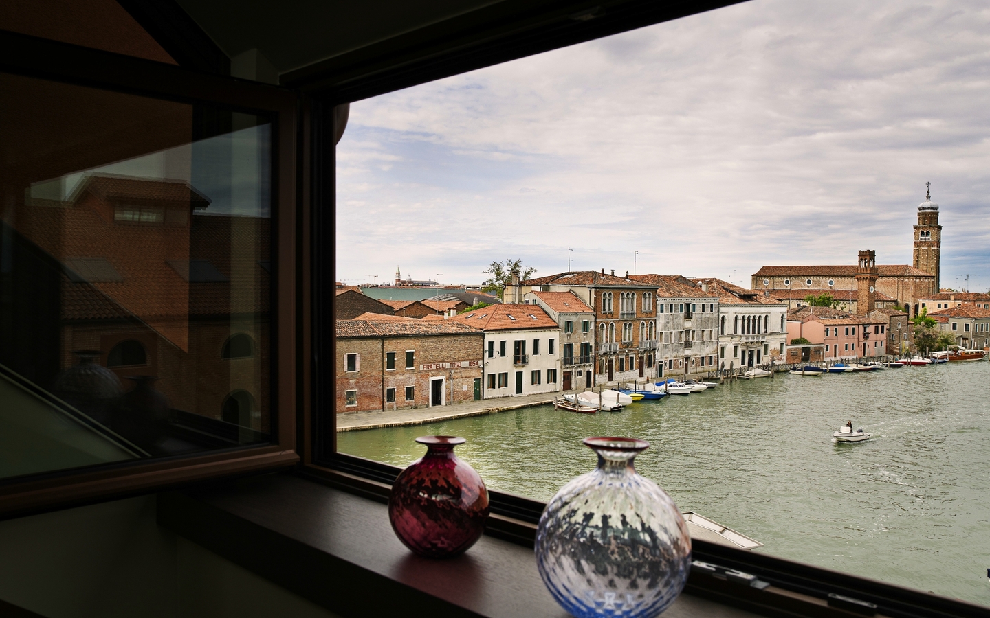 Blick aus einem Fenster auf Murano, Venedig, mit bunten Glasvasen im Vordergrund.