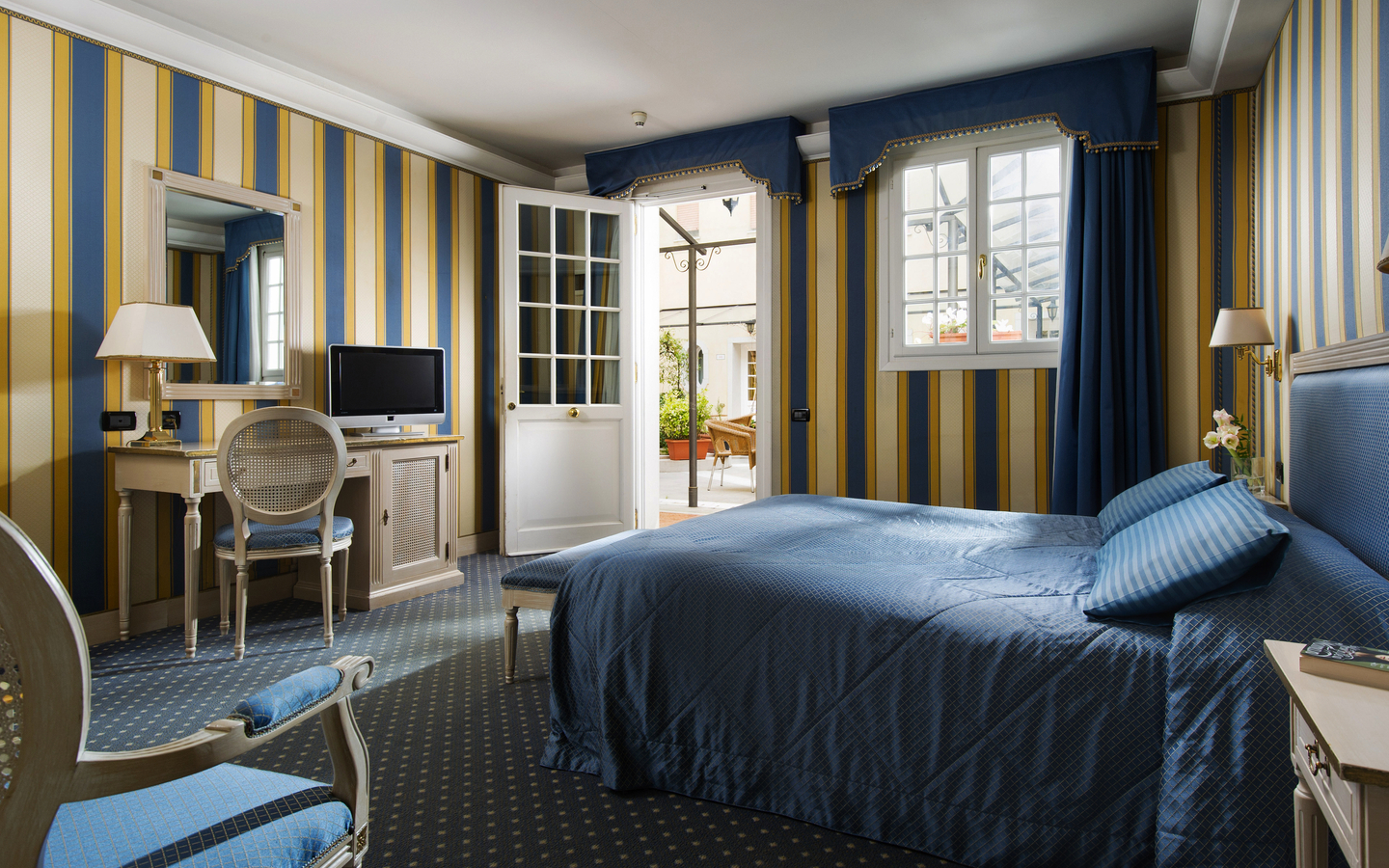 Hotelzimmer mit blauer Bettwäsche, TV, Schreibtisch und blick nach draußen.
