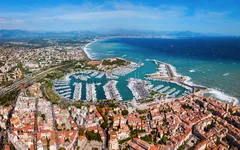 Luftaufnahme eines Küstenortes mit Yachthafen und Meer im Hintergrund.