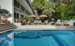 Hotel mit Pool und Liegestühlen, umgeben von Bäumen und Pflanzen in Cannes, Frankreich.