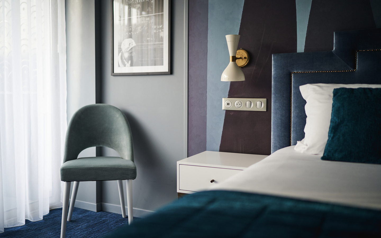 Hotelzimmer mit Doppelbett, Stuhl, Nachttisch und Wandlampe.