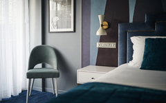 Hotelzimmer mit Doppelbett, Stuhl, Nachttisch und Wandlampe.
