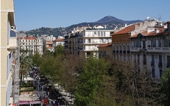 Straßenansicht einer französischen Stadt mit Häusern, Bäumen und Hügel im Hintergrund.
