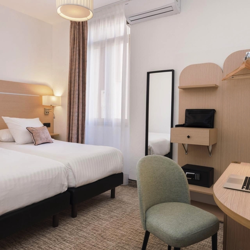 Modernes Hotelzimmer mit zwei Betten, Schreibtisch und Laptop.