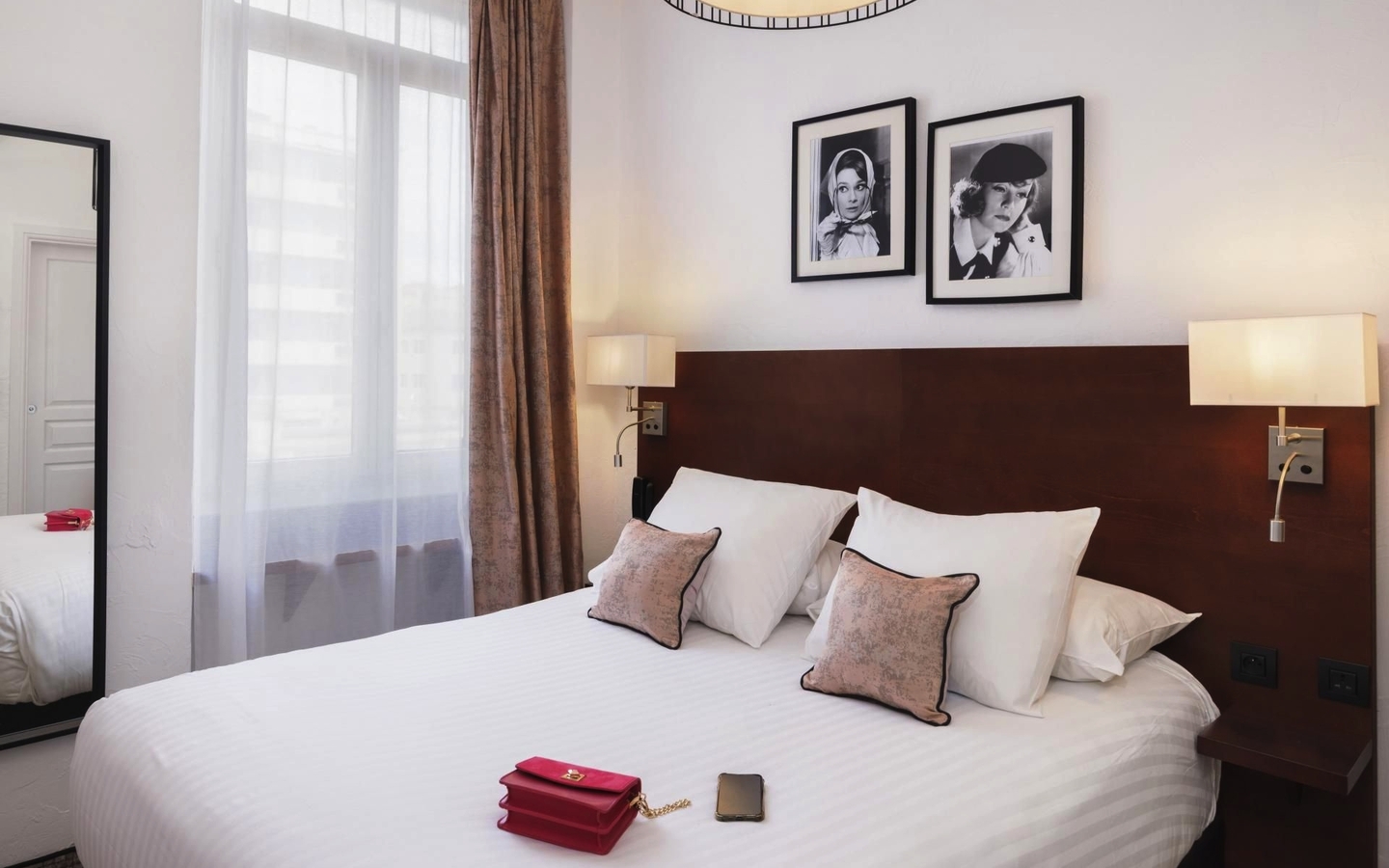Hotelzimmer mit Doppelbett, zwei Kissen, Nachttischen und Bildern an der Wand.