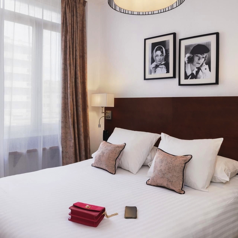Hotelzimmer mit Doppelbett, zwei Kissen, Nachttischen und Bildern an der Wand.