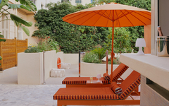 Zwei orange Liegestühle und Sonnenschirm auf Terrasse im Grünen