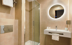 Modernes Badezimmer mit Dusche, rundem Spiegel und Waschbecken in neutralen Tönen.
