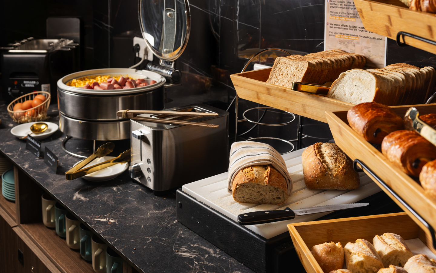 Frühstücksbuffet mit Brot, Gebäck und Warmhaltebehältern in einem Hotel in Nizza.