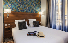 Hotelzimmer mit Doppelbett, dekoriert mit Kissen, Zeitschrift und Hut auf dem Bett.