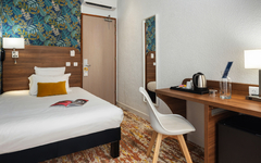 Einzelzimmer mit Bett, Holztisch, Stuhl, Wasserkessel und dekorativer Tapete.