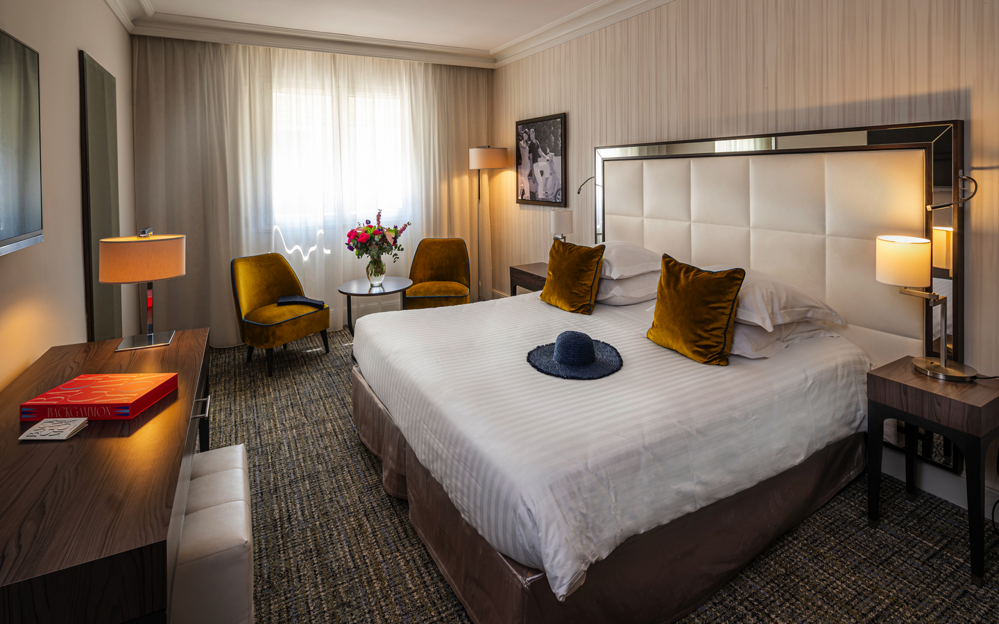 Hotelzimmer mit großem Bett, zwei Sesseln, Tisch und heller Fensterfront.