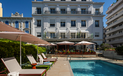 Sonnenterrasse und Pool vor einem Hotel in Cannes bei blauem Himmel.