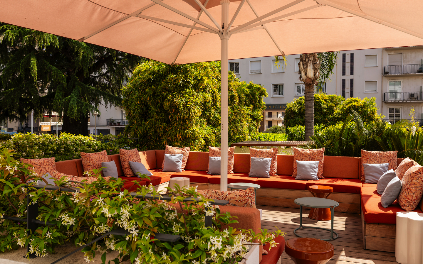 Sonniger Hotel-Loungebereich mit orangefarbenen Kissen und Sonnenschirm.