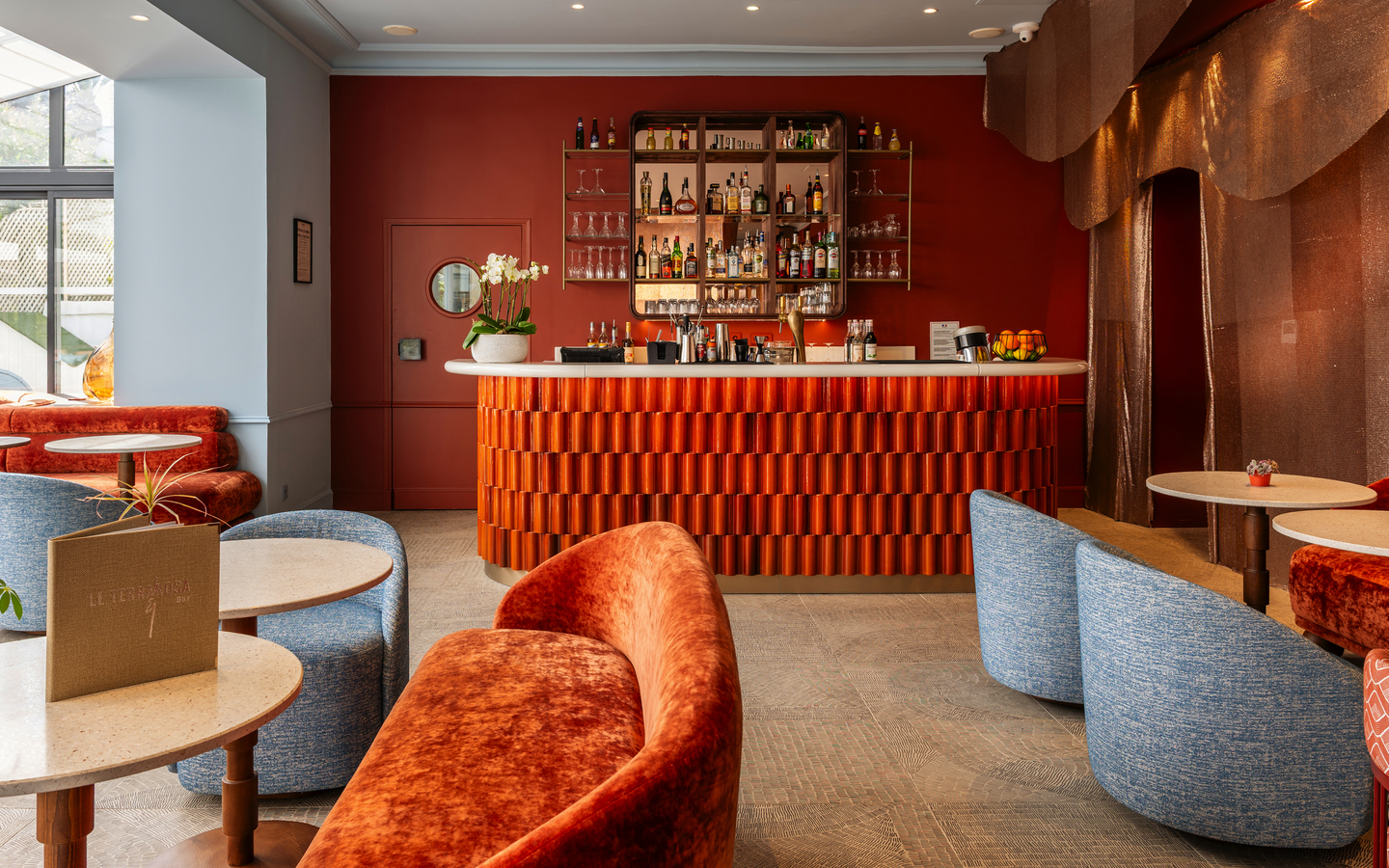 Barbereich im Hôtel Le Canberra mit roten und blauen Möbeln und gut bestückter Theke.