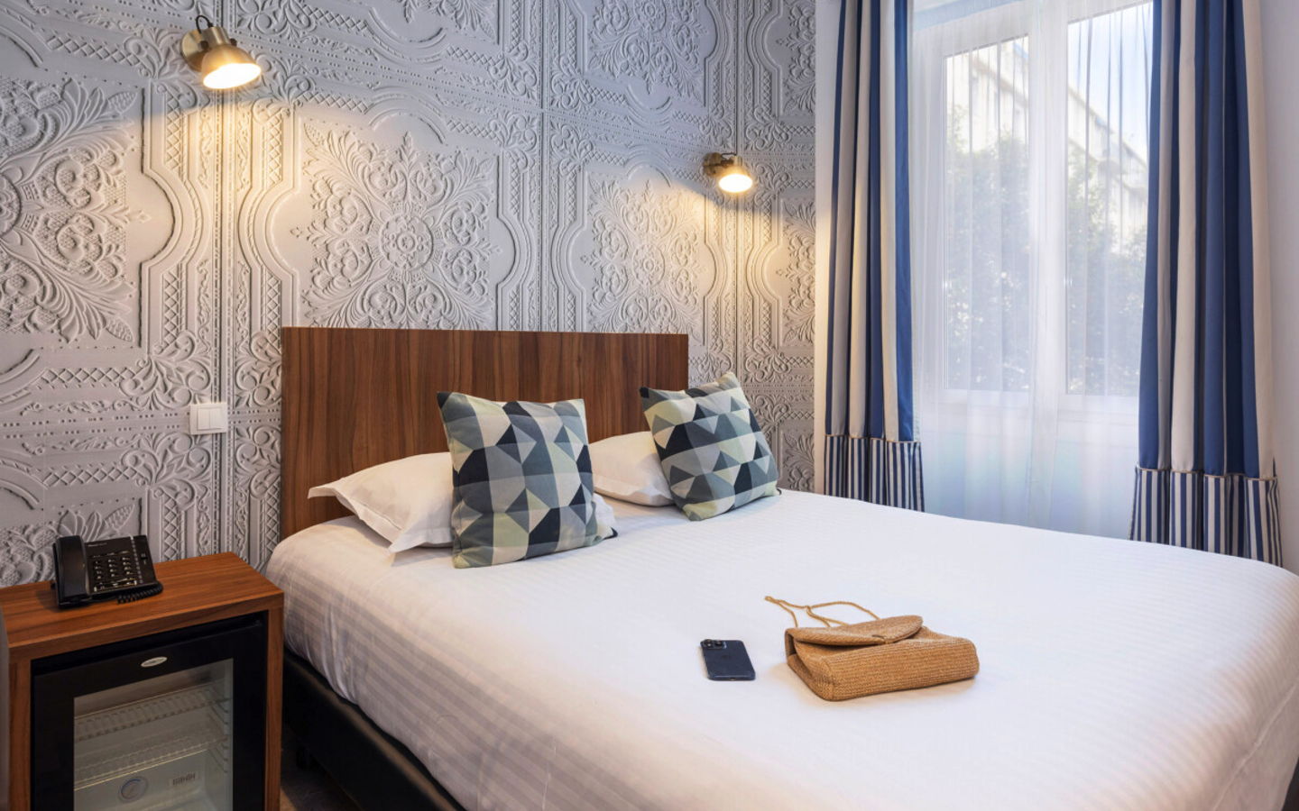 Klassisches Hotelzimmer mit Doppelbett, Wandbeleuchtung, Fenster und dekorativen Kissen.