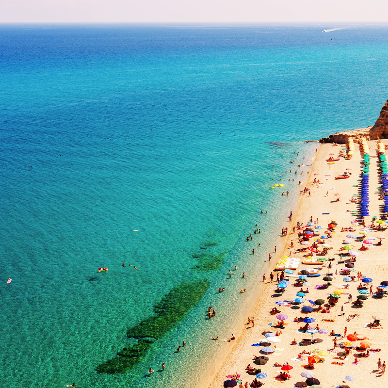 Sandstrand mit bunten Sonnenschirmen, Menschen im Meer und an der Küste.