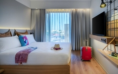 Modernes Hotelzimmer mit Doppelbett, Koffer und großem Fenster.
