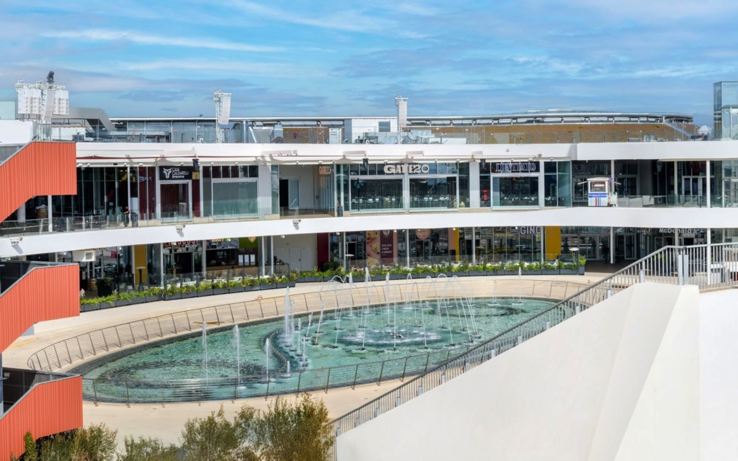 Gebäude mit Terrasse und runder Wasserskulptur im Vordergrund