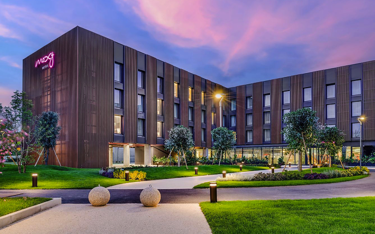 Hotel Moxy Pompeii bei Sonnenuntergang mit Garten und beleuchteten Wegen